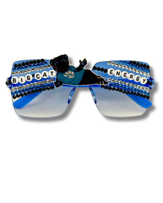 Blue and black rhinestone-studded novelty sunglasses with a black cat wearing a blue paw-print shirt on the front, and 'BIG CAT ENERGY' lettered across the lenses.