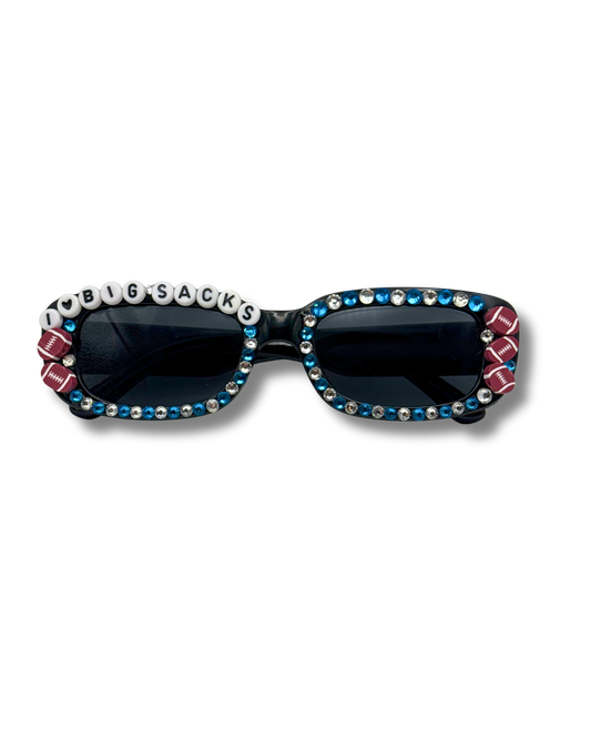 A pair of novelty sunglasses with dark lenses, decorated with silver rhinestones, blue rhinestones, football side accents, and white letter beads spelling 'I HEART BIG SACKS' on the top frame.