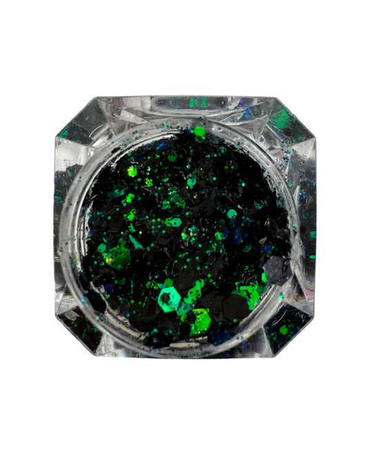 Top-down view of a clear faceted octagonal container filled with black glitter and vibrant green iridescent flakes, set against a plain white background.