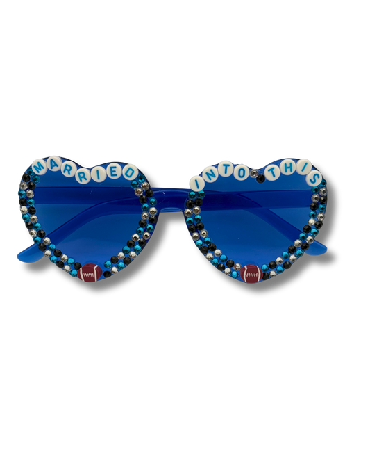 Heart-shaped novelty sunglasses with blue lenses, rhinestone borders, and white letter tiles spelling 'MARRIED INTO THIS' on a white background.