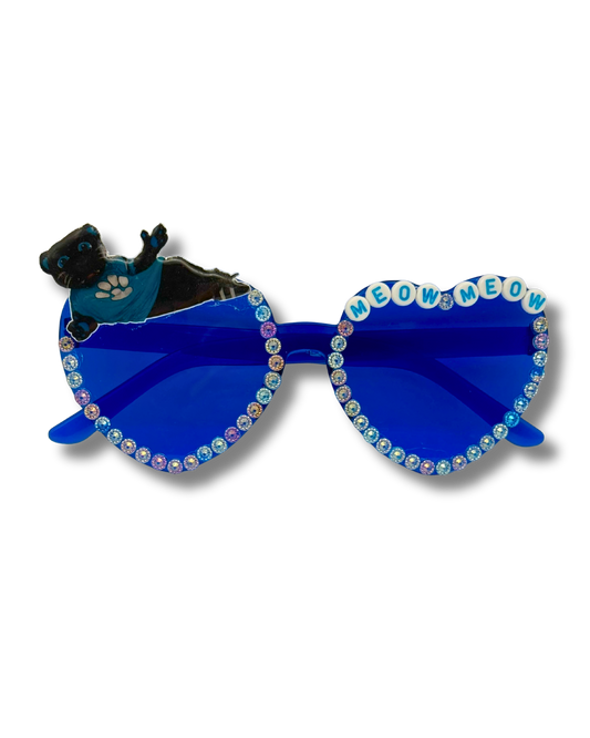 Blue heart-shaped sunglasses with rhinestone trim, featuring a black cat figurine on the left lens and the words 'MEOW MEOW' spelled out in cat-eye letters on the right lens.