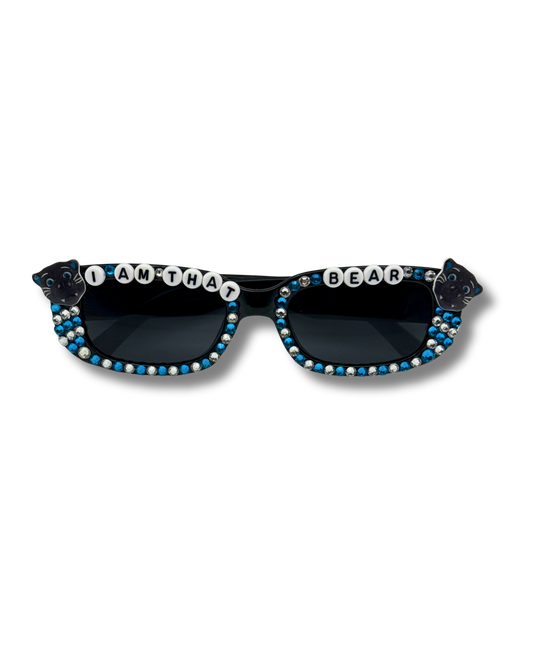 Black sunglasses with blue and white rhinestone embellishments, featuring 'I AM THAT BEAR' letter beads on the front frame and bear-shaped temple tips, shown against a plain white background.