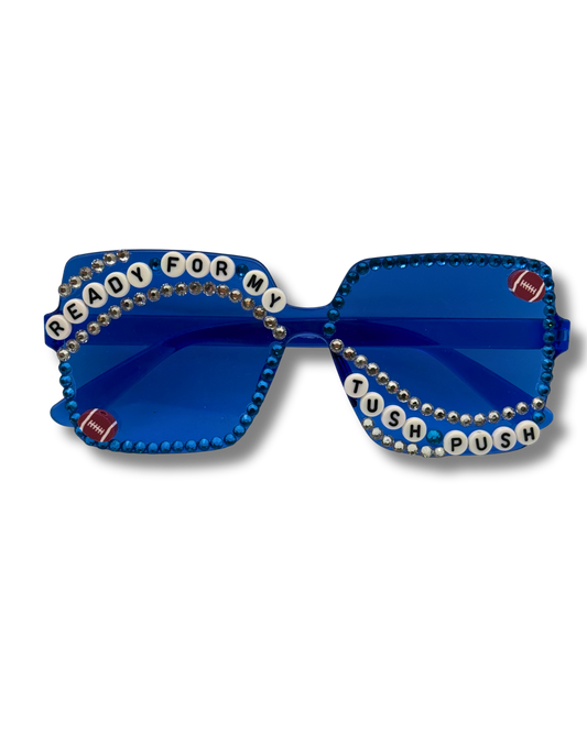 Blue rhinestone-studded novelty sunglasses with football-themed embellishments and letter beads spelling 'READY FOR MY TUSH PUSH'.